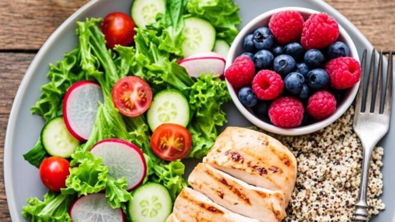 A vibrant, overhead flat-lay photograph of a well-balanced, high-volume meal on a rustic wooden table. The plate is large and filled with a colourful array of low-calorie-density foods: a generous portion of leafy green salad with cherry tomatoes, cucumber slices, and radishes, alongside a serving of grilled chicken breast, a scoop of quinoa, and a small bowl of fresh berries. A glass of water with lemon slices and a sprig of mint sits beside the plate. The lighting is natural and bright, evoking a sense of freshness and abundance, visually demonstrating that a calorie-conscious meal can be plentiful and satisfying.